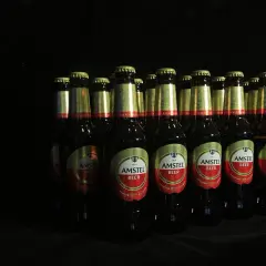 Rząd butelek piwa Amstel na czarnym tle. Czy picie piwa podnosi ciśnienie? To pytanie pozostaje otwarte.