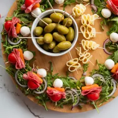 Oto pomysł, jak udekorować przystawki: kolorowe szaszłyki z pomidorkami, mozzarellą, salami i warzywami na desce z oliwkami i serem.