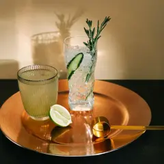 Orzeźwiający drink z limonką, lodem i rozmarynem. Obok drugi napój i złota miarka.