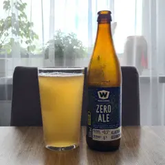 Szklanka i butelka piwa bezalkoholowego "Zero Ale" na drewnianym stole. Etykieta informuje, co zawiera piwo bezalkoholowe: ekstrakt 6%, alkohol ≤0.5%.