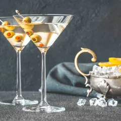 Dwa kieliszki z martini, ozdobione oliwkami, czekają na degustację. Obok lód i cytryna, idealne dodatki, by dowiedzieć się, jak pić martini.
