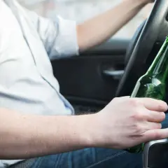 Mężczyzna za kierownicą trzyma butelkę piwa. Nie warto wiedzieć, ile % ma piwo, gdy prowadzisz.