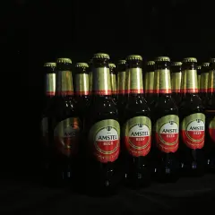 Rząd butelek piwa Amstel na czarnym tle. Czy piwo jest niezdrowe? To zależy od ilości.