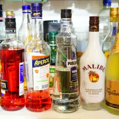 Na półce stoją butelki z różnymi alkoholami. Wśród nich wódka Puschkin, która ma 40% alkoholu, Aperol, Malibu i Freixenet.