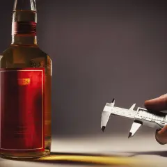 Precyzyjne mierzenie, ile etanolu jest w wódce, za pomocą suwmiarki cyfrowej obok butelki.