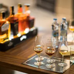 Degustacja whisky, czy bimber to whisky? Butelki i kieliszki z bursztynowym trunkiem na drewnianym stole.