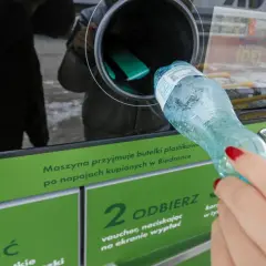 Kobieta wrzuca plastikową butelkę do maszyny przyjmującej opakowania.