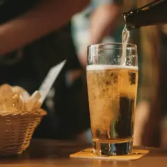 Złociste piwo IPA i APA leje się do szklanki. Obok koszyk z pieczywem.