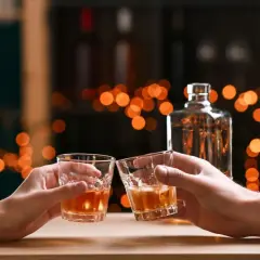 Dwie osoby wznoszą toast szklankami z bursztynowym płynem. Czysta wódka ma zero węglowodanów.
