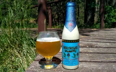 Piwo Delirium Tremens w szklance i butelce, na drewnianym tarasie wśród zieleni.