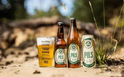 Szklanka i butelki z polskimi piwami typu lager "Pils" od Trzech Kumpli na piasku.