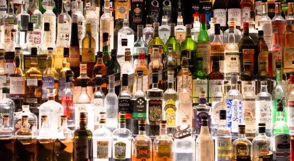 Rząd butelek alkoholi, w tym wódki, whisky i likierów, na półce.