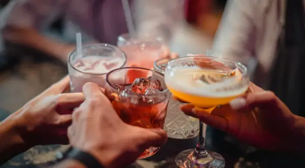 Ludzie wznoszą toasty kolorowymi drinkami z lodem.