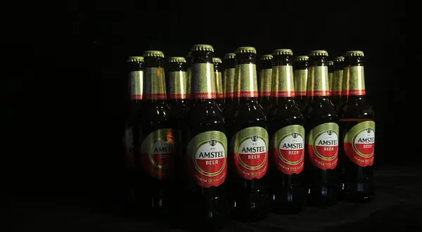 Rząd butelek piwa Amstel na czarnym tle. Czy picie piwa podnosi ciśnienie? To pytanie pozostaje otwarte.