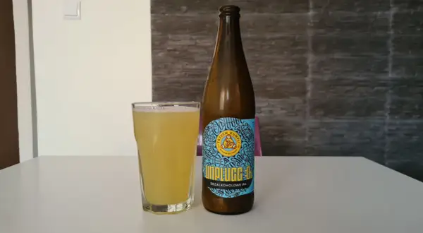 Szklanka i butelka piwa miodowego bezalkoholowego Unplugged IPA na białym stole.