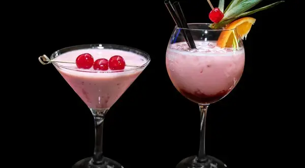 Dwa różowe drinki, jeden w kieliszku martini z wiśniami, drugi w kieliszku typu goblet z owocami. Zastanawiasz się, ile kalorii ma wódka smakowa?