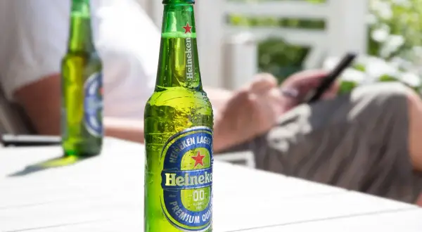 Orzeźwiające piwo bez cukru Heineken 0.0 na stole, w tle osoba korzystająca z telefonu.