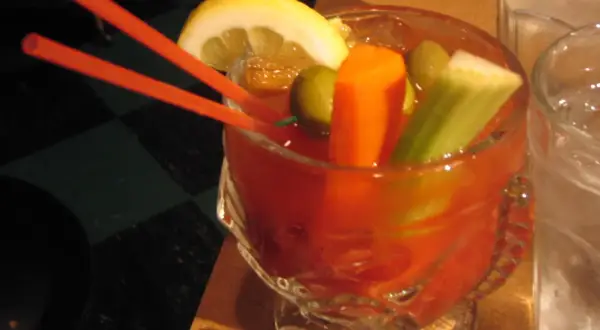 Krwawa Mery przepis: czerwony drink z cytryną, oliwkami, selerem i marchewką, podany z pomarańczowymi słomkami.