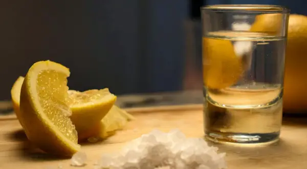 Składniki na vodka sour przepis: kieliszek wódki, cytryna i sól na desce.