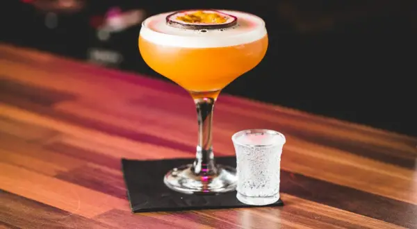 Pomarańczowy koktajl Pornstar Martini z owocem marakui i kieliszek szampana. Idealny sposób, by zacząć wieczór.