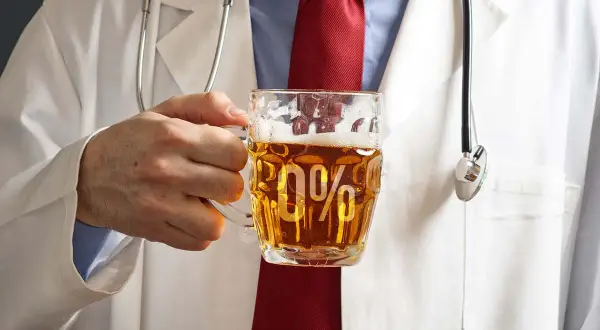 Lekarz w białym kitlu trzyma kufel piwa bezalkoholowego z napisem "0%". Czy piwo bezalkoholowe podnosi ciśnienie?