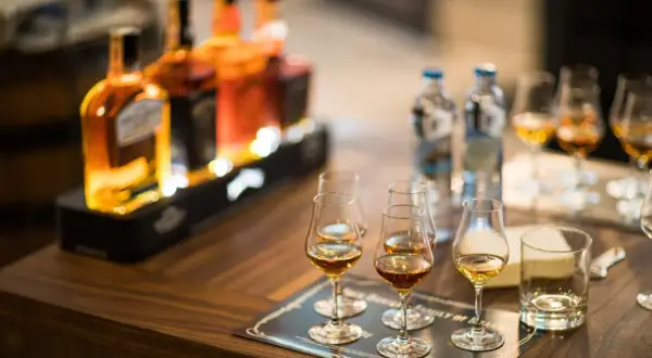 Degustacja whisky, czy bimber to whisky? Butelki i kieliszki z bursztynowym trunkiem na drewnianym stole.