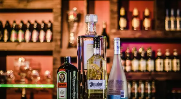 Butelki Jägermeister, El Jimador, Absolut i Hipnotiq na tle baru.