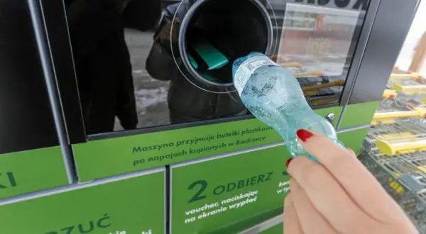 Kobieta wrzuca plastikową butelkę do maszyny przyjmującej opakowania.