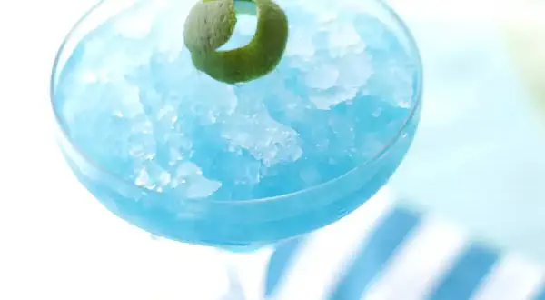 Orzeźwiający drink Błękitna Laguna, zmrożony i udekorowany skórką limonki, idealny na upalne dni.