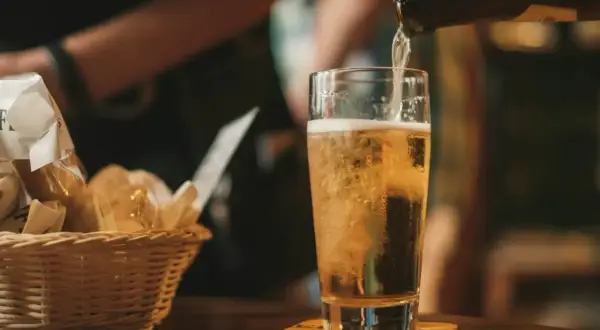 Złociste piwo IPA i APA leje się do szklanki. Obok koszyk z pieczywem.