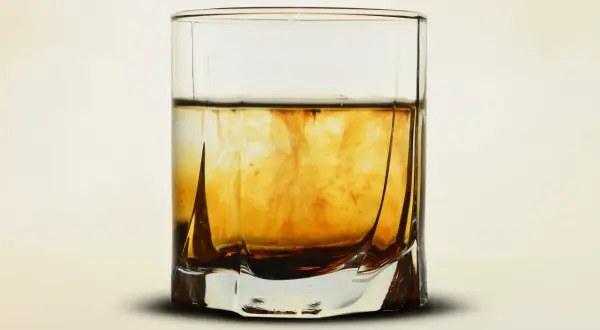 Szklanka z bursztynowym płynem, w którym rozpuszcza się barwnik. Wizualizacja procesu, jak zrobić whisky w domu.