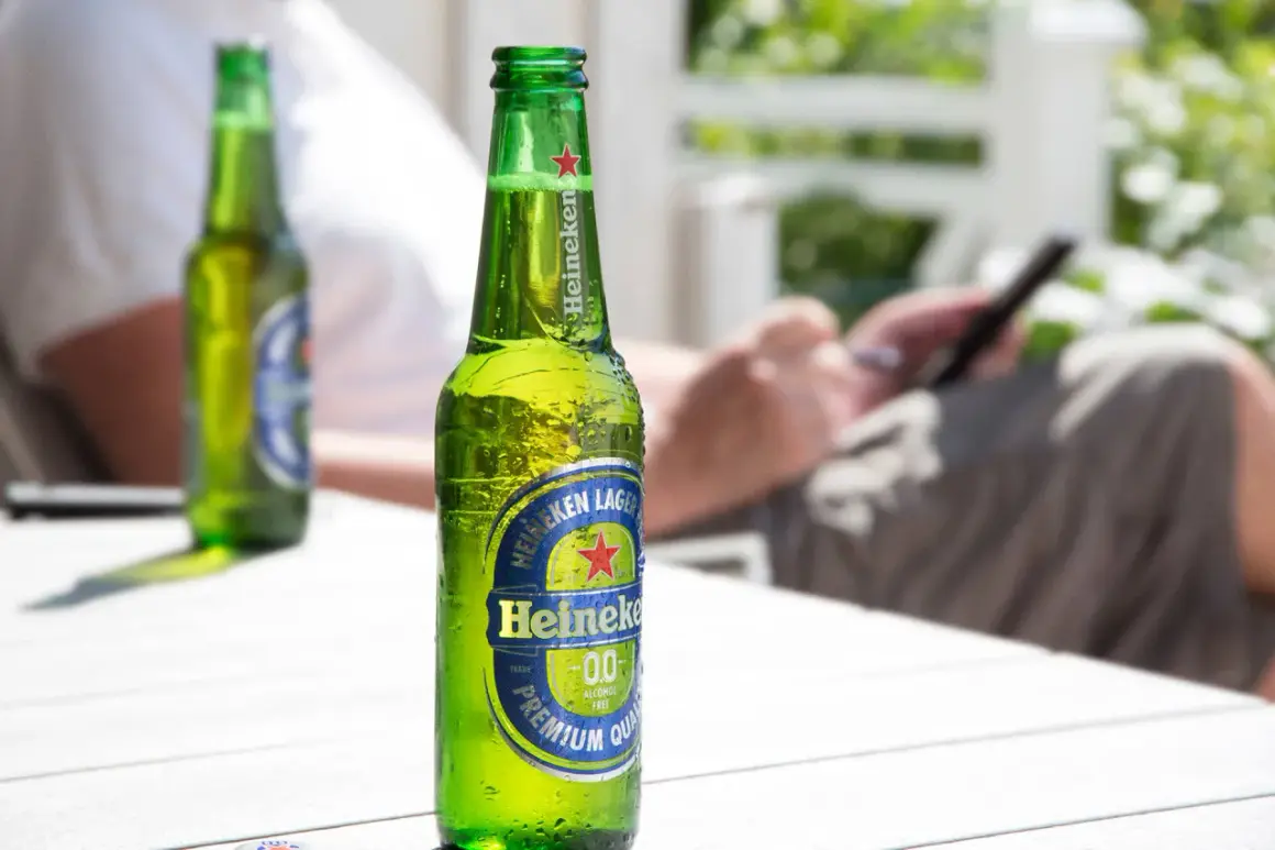 Orzeźwiające piwo bez cukru Heineken 0.0 na stole, w tle osoba korzystająca z telefonu.