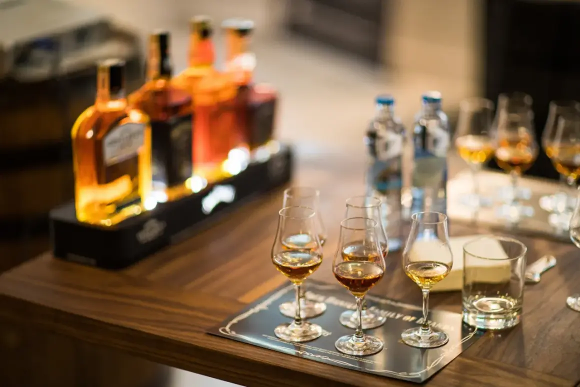 Degustacja whisky, czy bimber to whisky? Butelki i kieliszki z bursztynowym trunkiem na drewnianym stole.