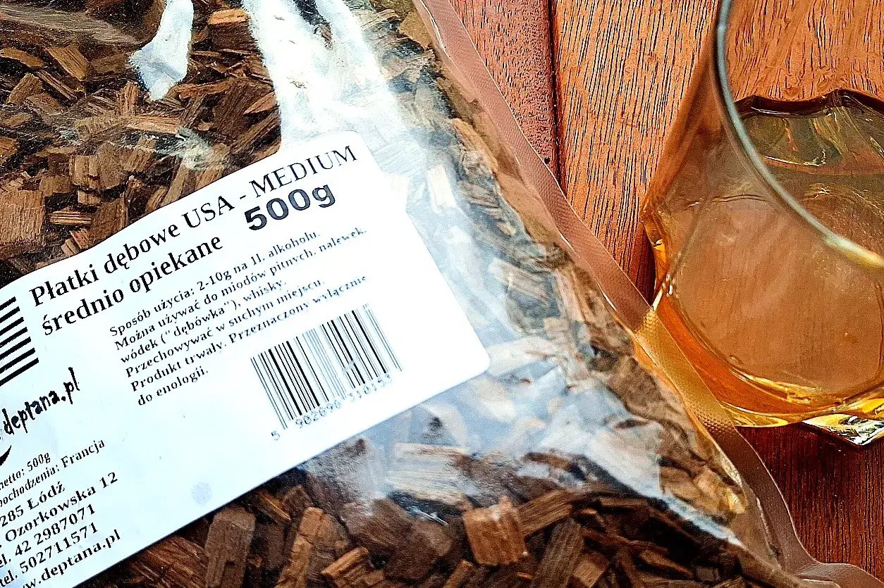 Płatki dębowe do wędzenia, idealne, by dowiedzieć się, jak zrobić whisky w domu. W tle szklanka z bursztynowym trunkiem.