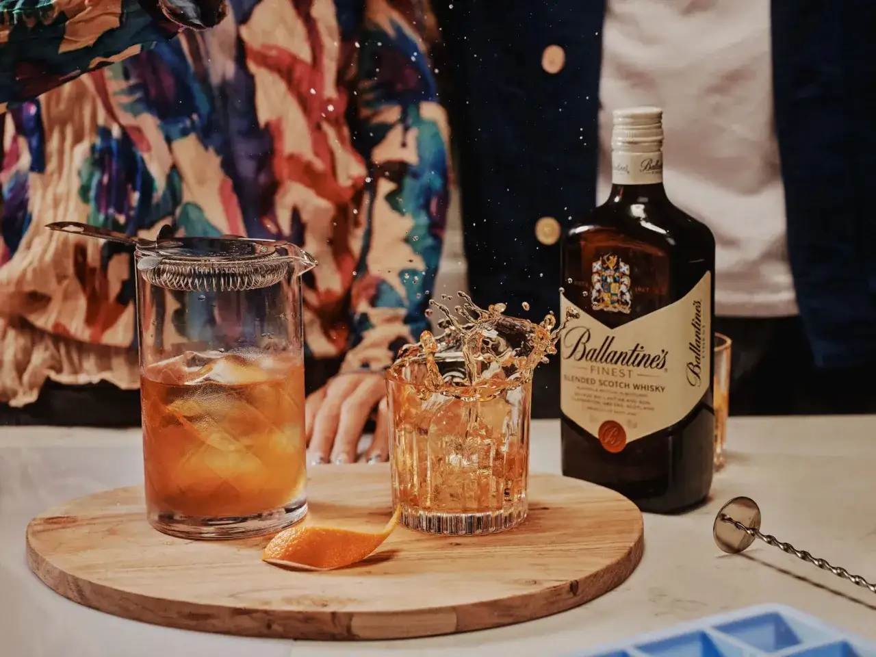 Jak pić Ballantines? Z lodem i skórką pomarańczy, w towarzystwie butelki i akcesoriów barmańskich.